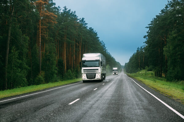 White Truck Or Tractor Unit, Prime Mover, Traction Unit In Motion On Road, Freeway. Asphalt Motorway Highway Against Background Of Forest Landscape. Business Transportation And Trucking Industry